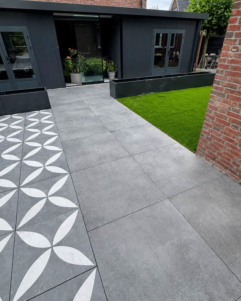Terras met grote grijze tegels en een sierpatroon, met kunstgras en een tuinhuis