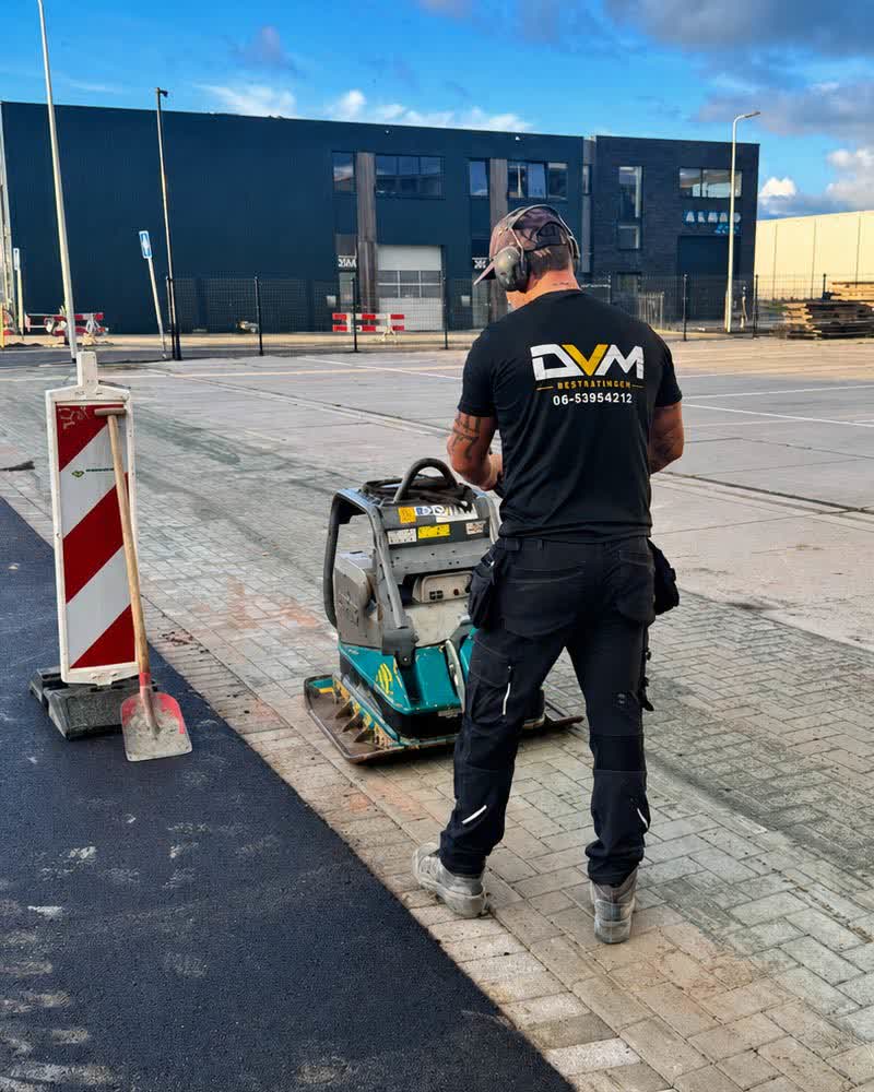 Medewerker van DVM Bestratingen trilt de bestrating aan bij een bedrijfspand